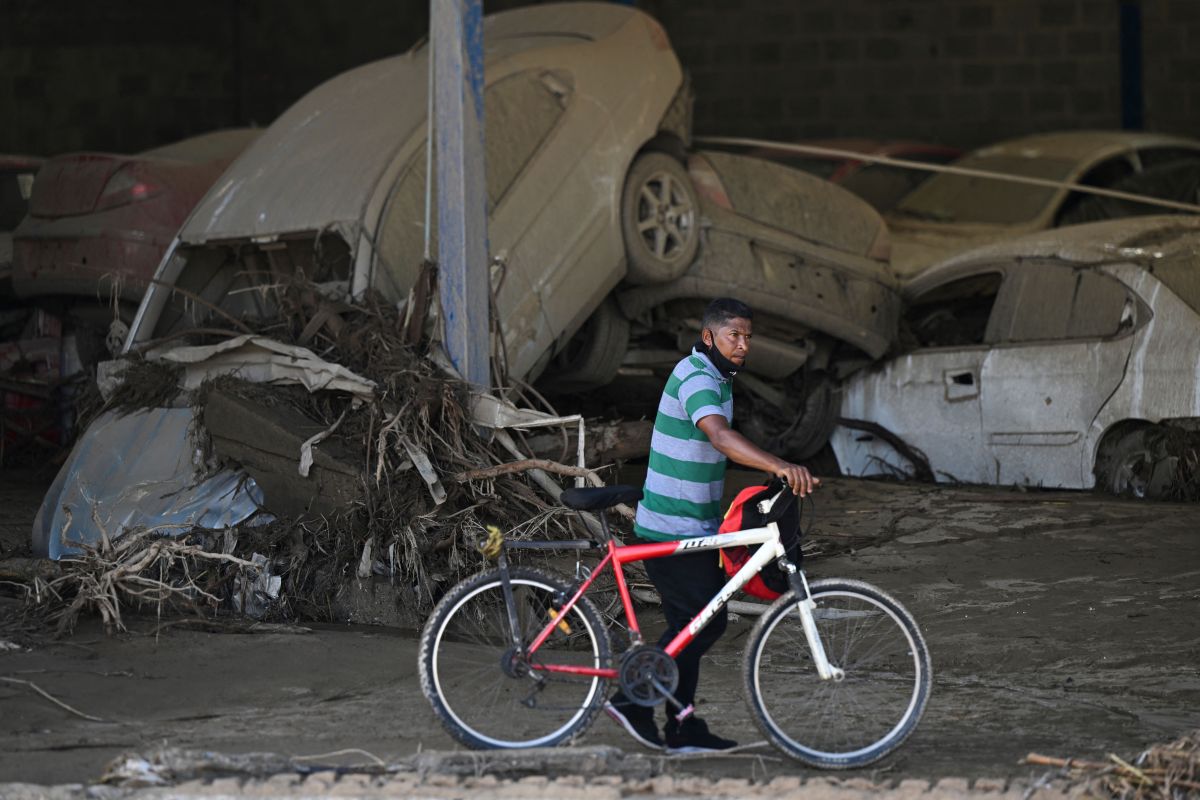 A man with his bicycle passes in front of damaged cars from a vehicle assembly company after a landslide during heavy rains in Las Tejerias, Aragua state, Venezuela, on October 10, 2022. - A landslide in central Venezuela left at least 22 people dead and more than 50 missing after heavy rains caused a river to overflow, Vice President Delcy Rodriguez said Sunday. (Photo by Yuri CORTEZ / AFP) (Photo by YURI CORTEZ/AFP via Getty Images)